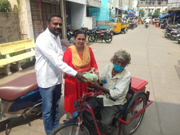 Handing food parcels to an elderly man on a cycle rickshaw in a street
