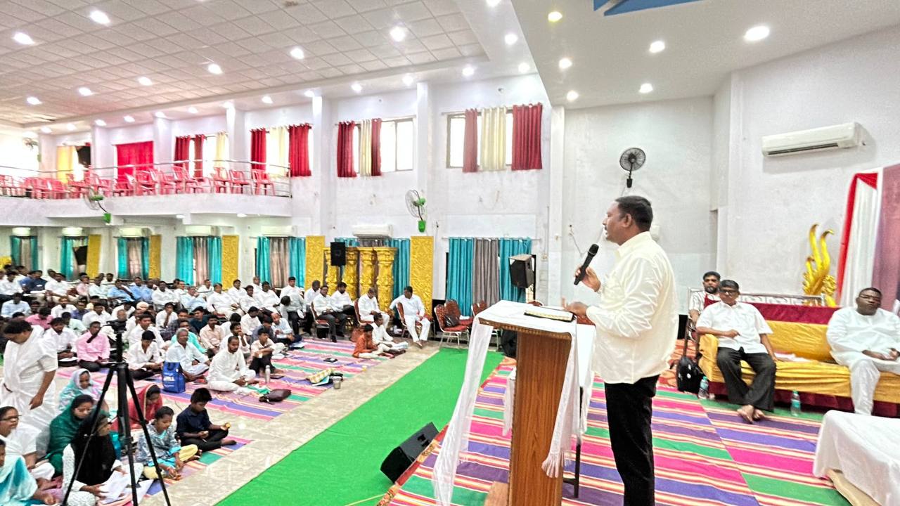 A speaker at the pulpit addressing a full hall during a ministry gathering